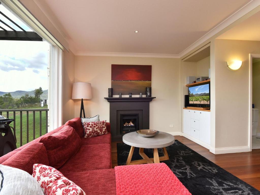 uma sala de estar com um sofá vermelho e uma lareira em Villa 2br Moscato Villa located within Cypress Lakes Resort em Pokolbin