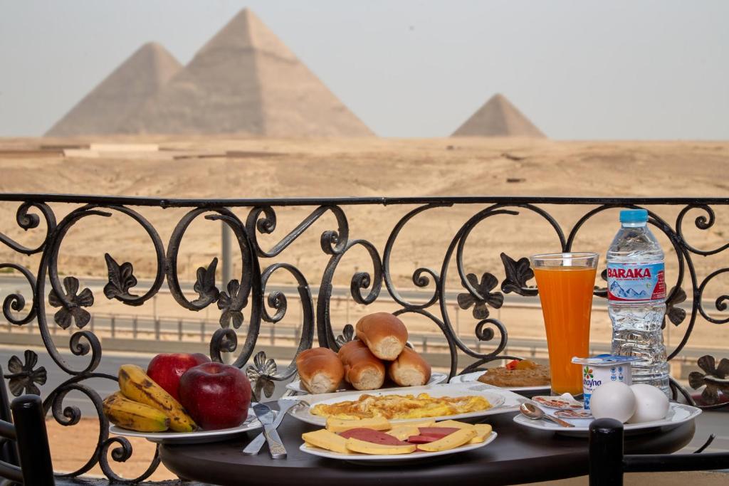 une table avec des assiettes de nourriture et de boissons et des pyramides dans l'établissement Pyramids Planet Hotel, au Caire