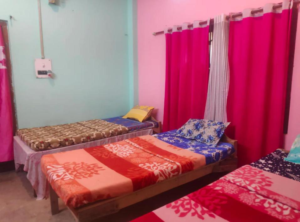 three beds in a room with pink curtains at Traveller's Nest Homestay in Siliguri