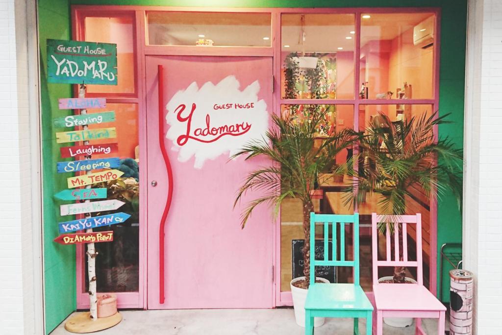 a pink door with two chairs in front of a store at Guest House Yadomaru in Osaka