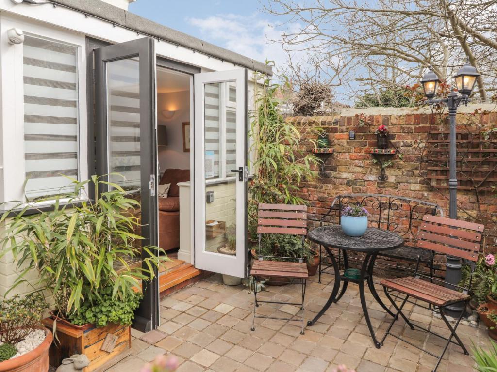 een patio met een tafel en stoelen naast een bakstenen muur bij Rose Cottage in Deal