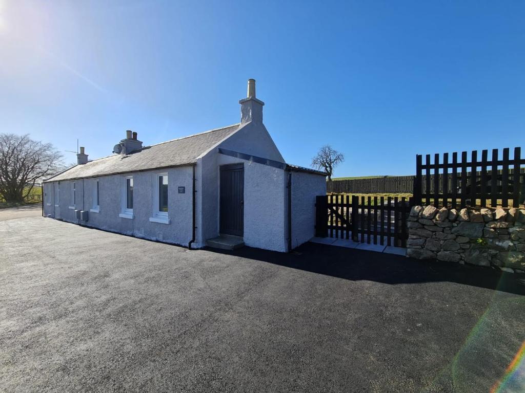 un edificio bianco con cancello e recinto di Bruxie Holiday Cottages - Honeysuckle Cottage a Maud