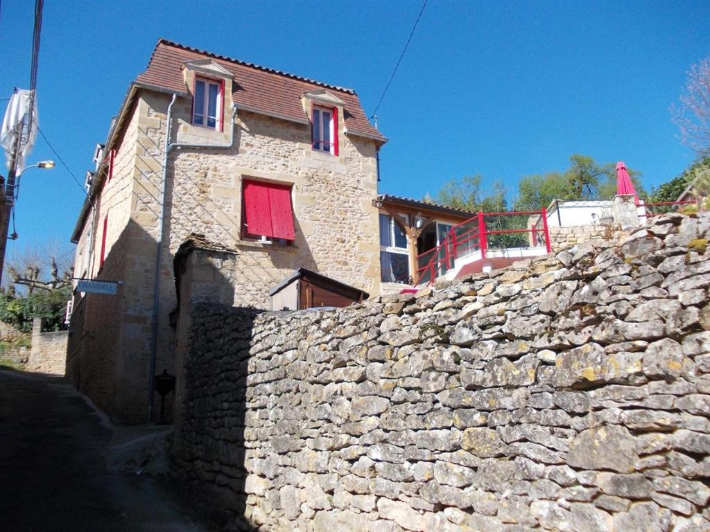 a stone house with red windows and a stone wall at Au Soleil Levant Homestay in Sarlat-la-Canéda