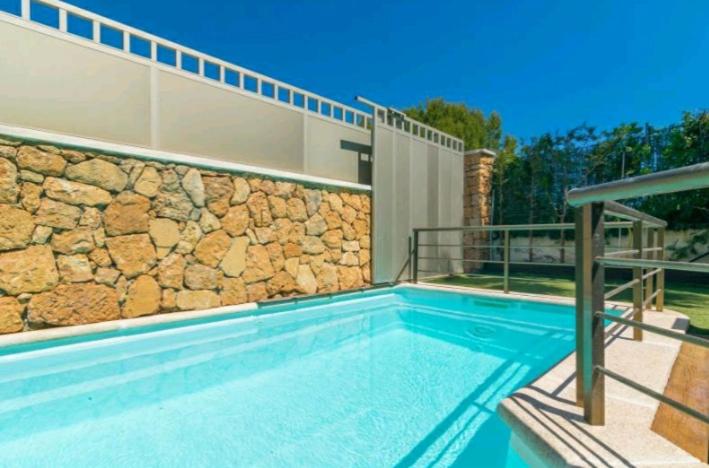una piscina con una pared de piedra junto a una casa en Bahamas 1 en Son Serra de Marina