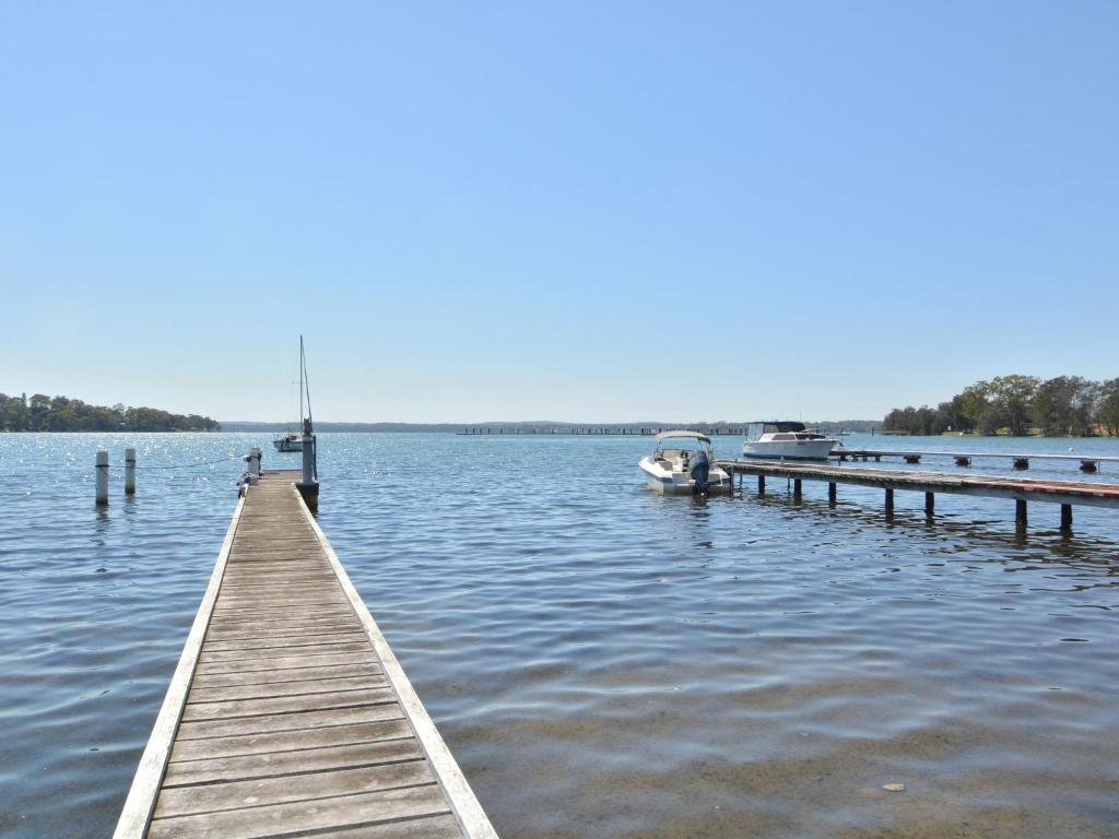 a dock on a lake with a boat in the water at Lake Macquaries' Edgewater Lakehouse at Morisset Memories in Morisset East