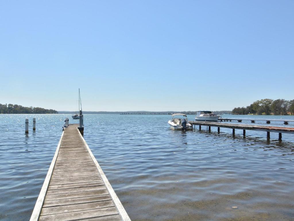 a dock on a lake with a boat in the water at Lake Macquaries' Edgewater Escape at Morisset Memories in Morisset