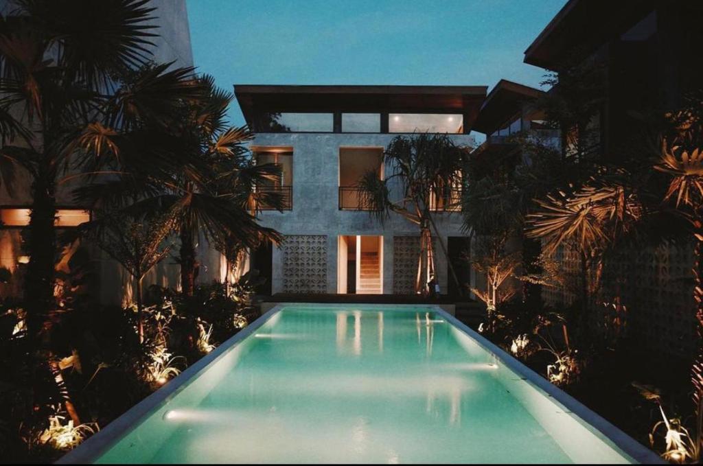 a swimming pool in front of a house with palm trees at T Lofts in Seminyak