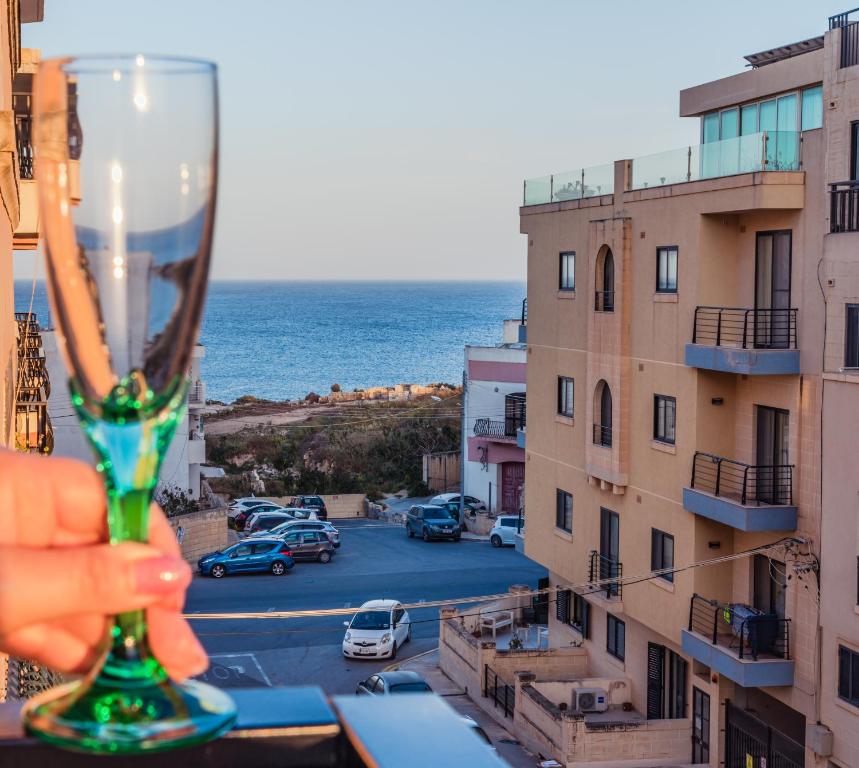 een hand met een wijnglas voor een stad bij Sea-View 3 bedroom Apartment - Sleeps 8 in Marsaskala