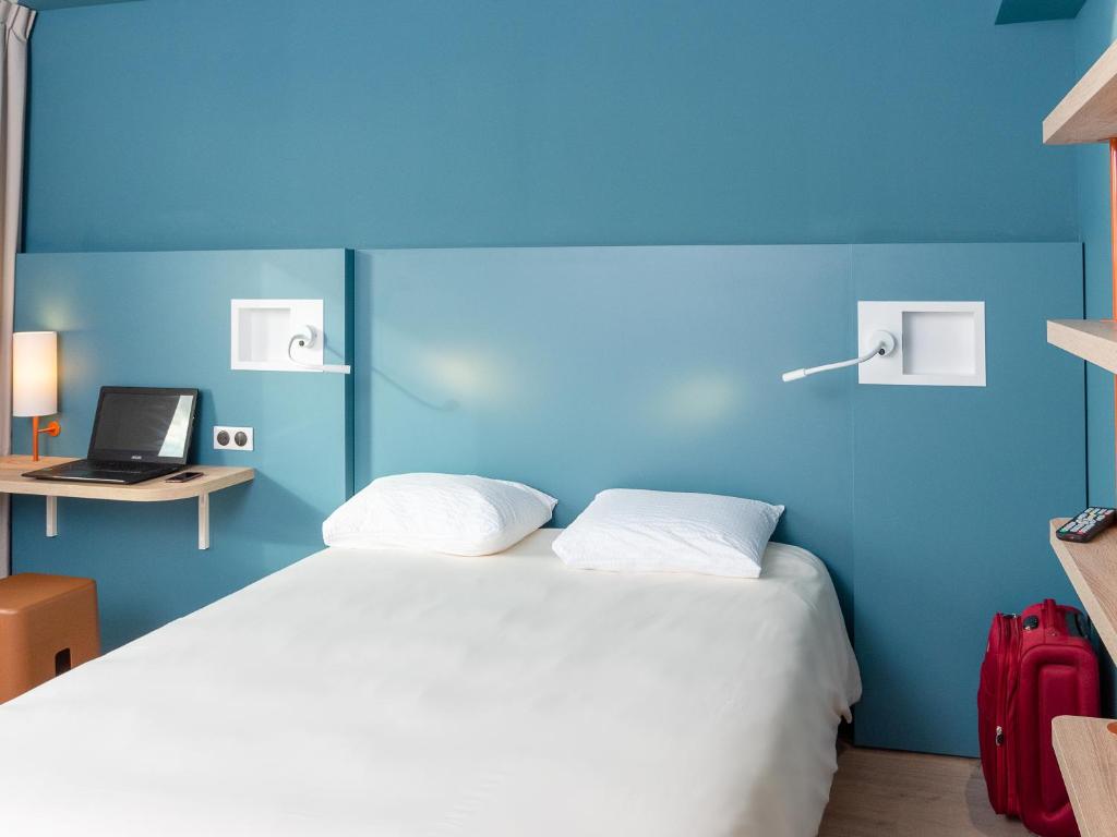 une chambre avec un lit blanc avec un mur bleu dans l'établissement ibis Budget Cognac, à Châteaubernard