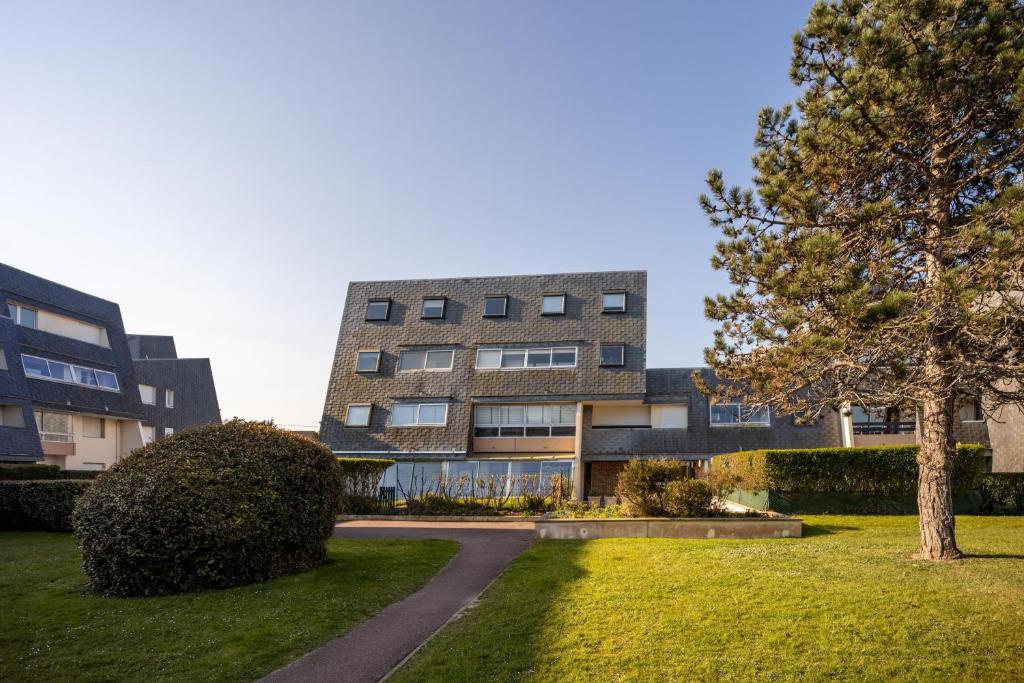 a building with a tree in front of a yard at Le Pavois - appartement à 50 mètres de la mer in Bernières-sur-Mer