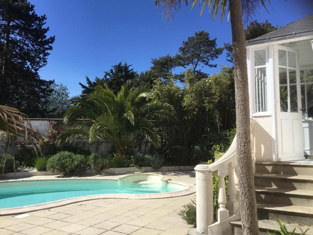 - une piscine à côté d'une maison avec un palmier dans l'établissement La Maison rose, à Portbail