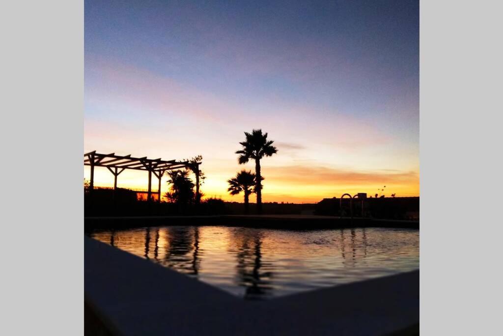 a sunset over a swimming pool with palm trees at Quinta dos Malhadais, Figueira - Farm house in Portimão