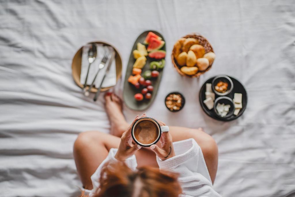 a woman sitting on a bed with a cup of coffee and food at Bio Habitat Hotel in Armenia