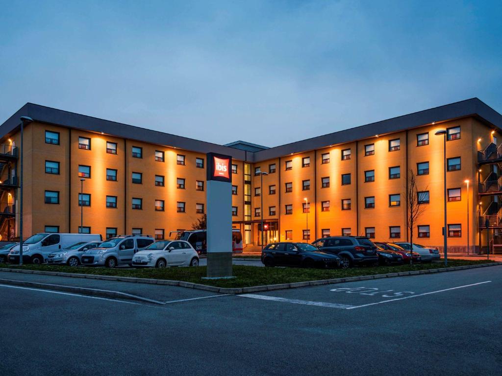 un gran edificio con coches estacionados en un estacionamiento en Hotel Ibis Milano Malpensa, en Cardano al Campo