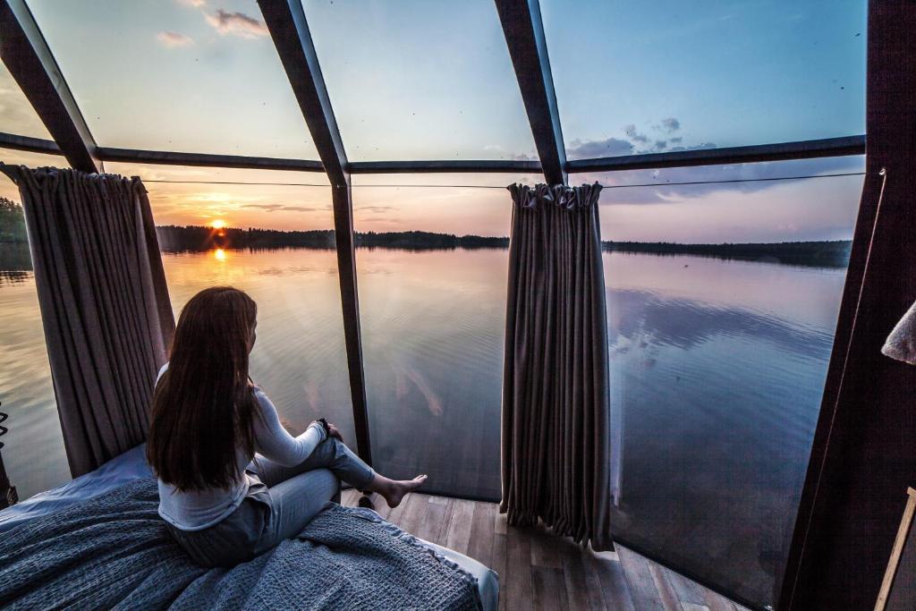 uma mulher sentada numa cama olhando para fora de uma janela para a água em Peace & Quiet Hotel em Jokkmokk