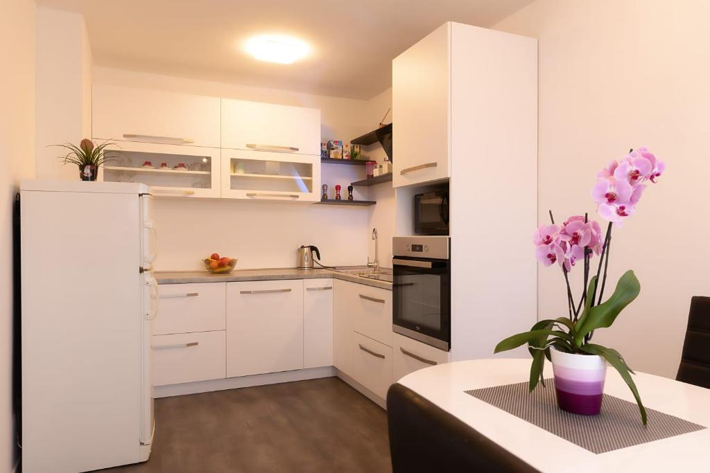 uma cozinha com armários brancos e uma mesa com um vaso de flores em Apartman MELANI em Slunj