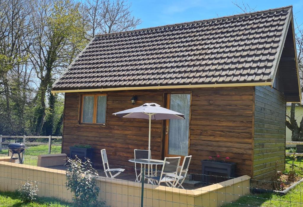 una pequeña casa de madera con mesa y sombrilla en La Cabane de Fierville, en Fierville-les-Parcs