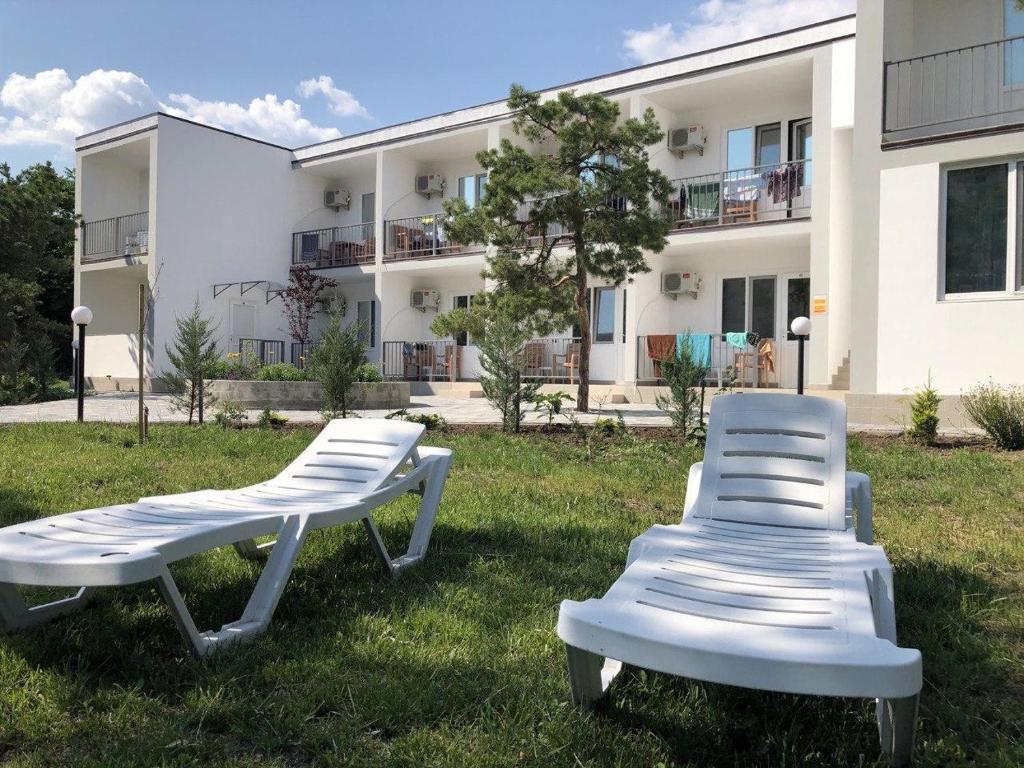 zwei weiße Stühle im Gras vor einem Gebäude in der Unterkunft Ассоль in Koblewe