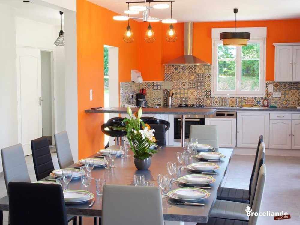 a dining room with a long table with chairs and a kitchen at Gite Les Gobelins in Paimpont