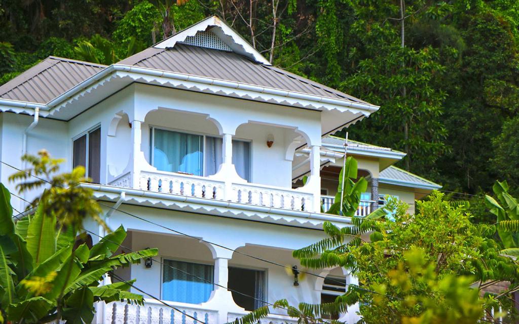 a white house with a balcony and trees at Saria Self Catering in Praslin
