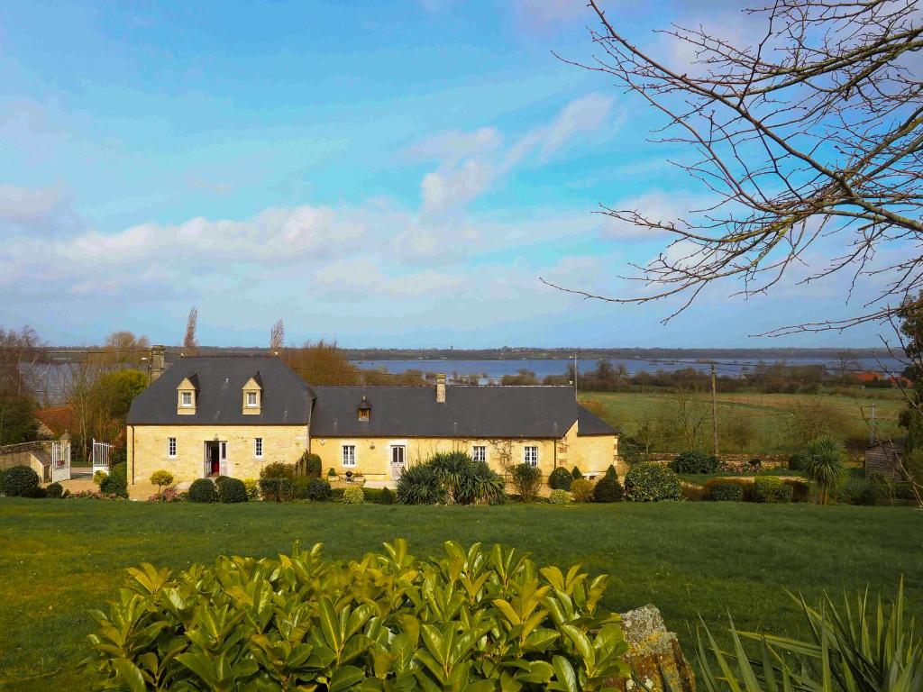 a large house on a green field with a lake in the background at Le domaine des Roseraies in Monfréville