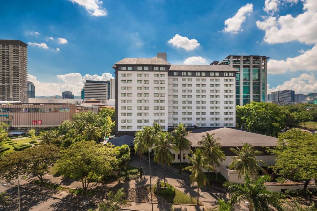 a large white building with palm trees in front of a city at Seda Ayala Center Cebu in Cebu City