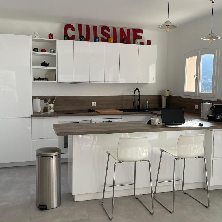 a kitchen with white cabinets and a counter with stools at Villa Turquoise Sagone in Sagone