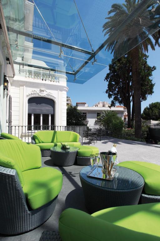 un patio avec des chaises et des tables vertes et un bâtiment dans l'établissement Villa Garbo, à Cannes