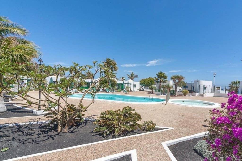 a swimming pool with palm trees and purple flowers at Bandama 15 2 Bedroom Ground Floor in Los Pocillos