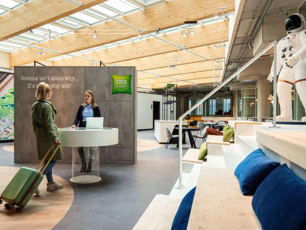 a woman standing at a desk in a building with luggage at ibis Styles Delft City Centre in Delft