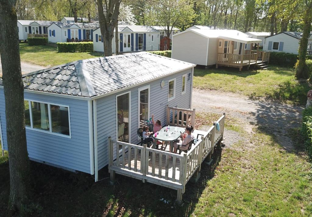 une petite maison bleue avec des personnes assises sur une terrasse couverte dans l&#39;établissement Camping le Balcon de la Baie, à Saint-Marcan