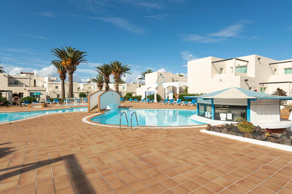 una piscina en un complejo con palmeras y edificios en HomeForGuest Apartamento 13 con terraza y piscina en Corralejo en Corralejo