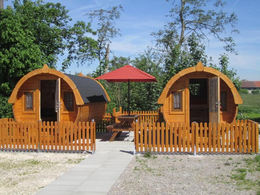 eine Holzhütte mit einem Zaun und einem Tisch in der Unterkunft Schlaffass-Camping Gutshof Donauried in Günzburg