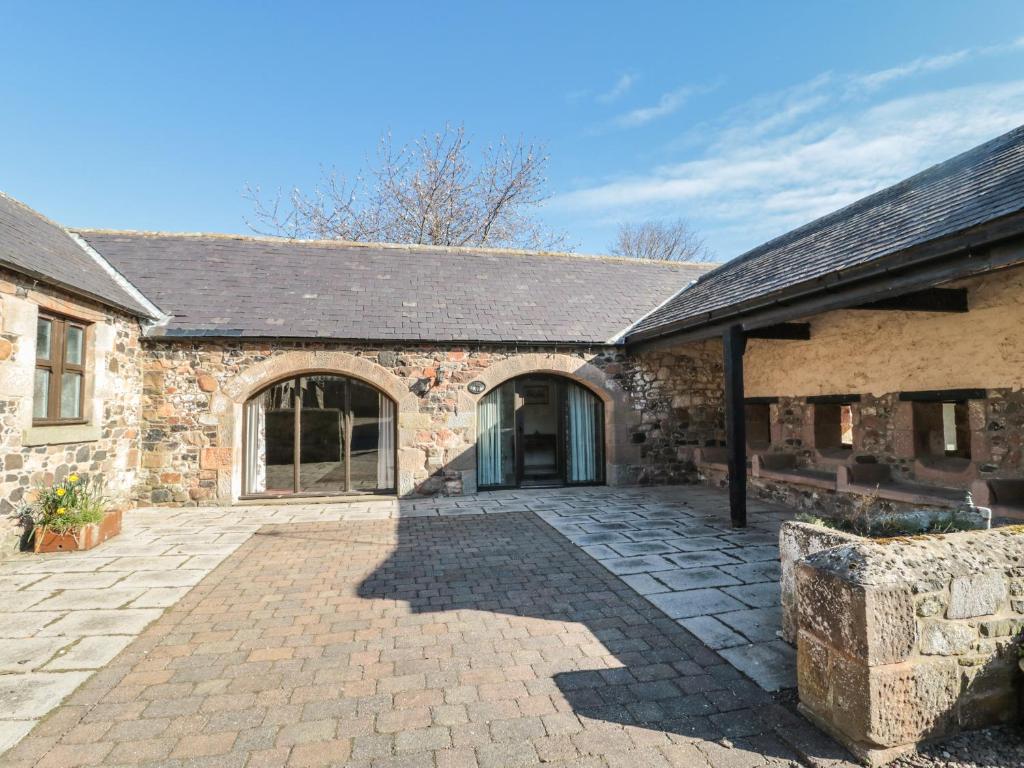 an old stone building with a large patio at Fern Cottage in Wooler