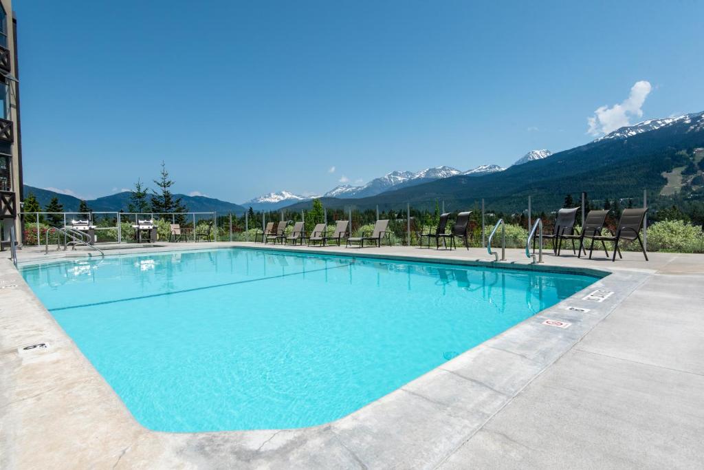 una piscina con sillas y montañas en el fondo en The Ironwood on Blueberry Hill, en Whistler