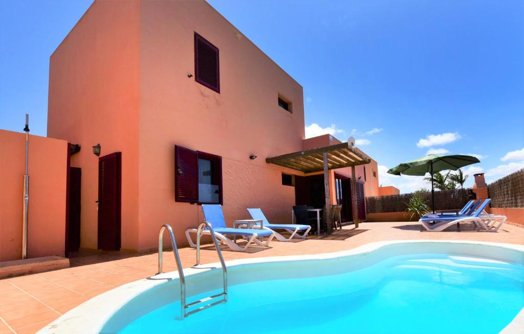 a pool in front of a house with chairs and an umbrella at Fuerteventura Sol Deluxe Villas in La Oliva