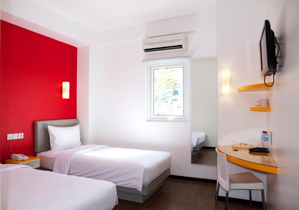a room with two beds and a desk and a window at Amaris Hotel Ambon in Ambon