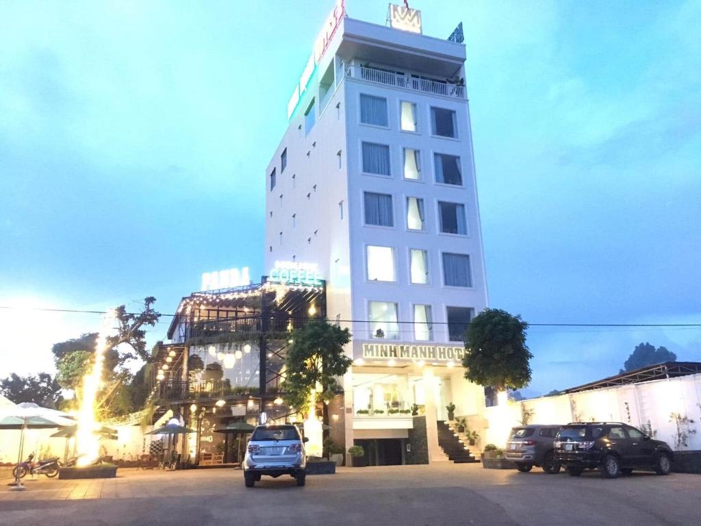 a tall white building with cars parked in a parking lot at Minh Manh Hotel 2 in Pleiku