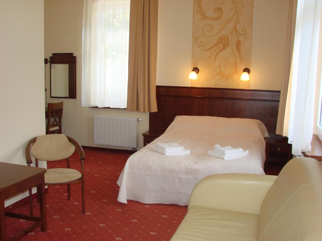Double hotel bedroom with made bed, folded towels, wooden headboard, seating area, warm ambient lighting.