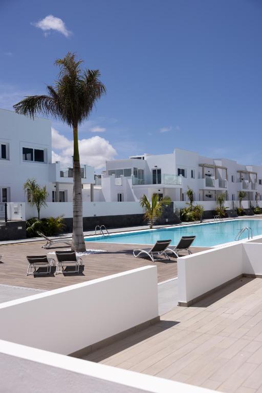 a swimming pool with a palm tree and white buildings at Island Home Fuerteventura in Corralejo