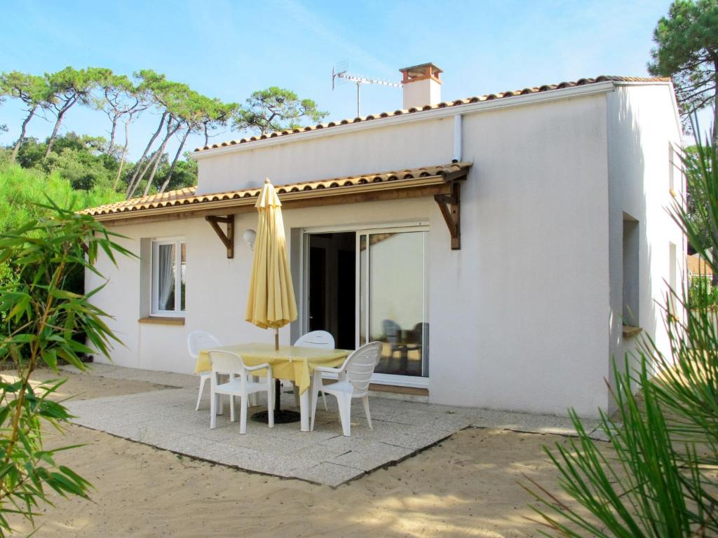 ein weißes Haus mit einem Tisch, Stühlen und einem Sonnenschirm in der Unterkunft Holiday Home Les Etrilles by Interhome in La Tranche-sur-Mer