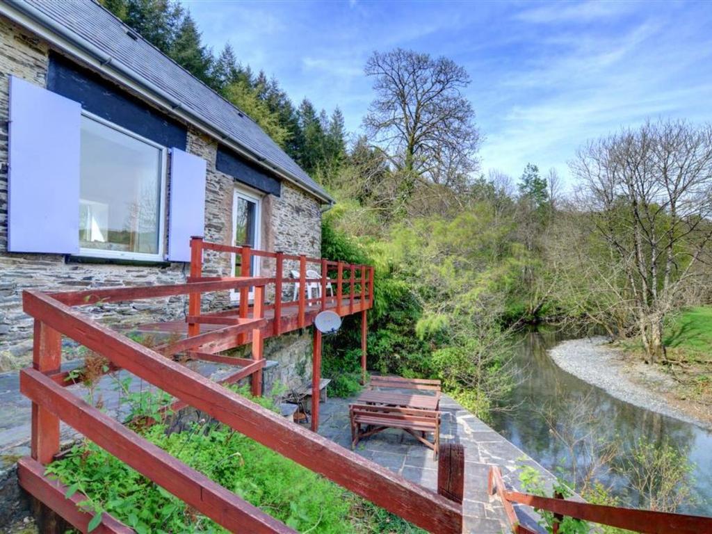 a house with a red deck next to a river at Holiday Home Pantperthog by Interhome in Esgair-geiliog