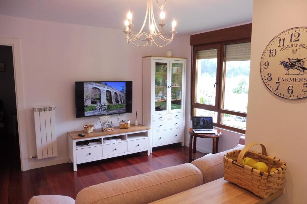 ein Wohnzimmer mit einem Sofa, einem TV und einer Uhr in der Unterkunft Casa Santolaya in Santiurde de Toranzo