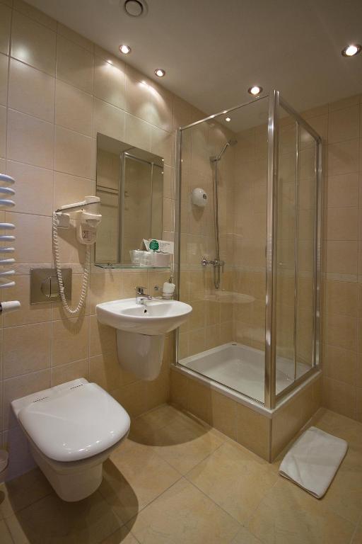 Compact hotel bathroom with glass shower enclosure, wall-mounted sink, toilet and coiled hairdryer.