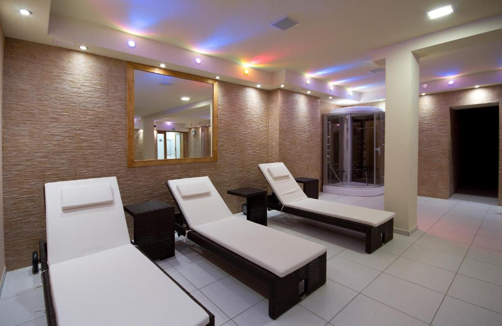 Spa relaxation room with three white cushioned lounge chairs, mosaic wall, colored ceiling lights.