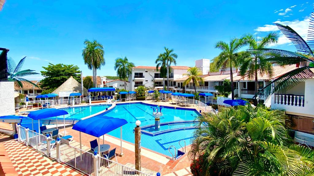 a resort pool with blue umbrellas and palm trees at Alborada Hotel Melgar in Melgar