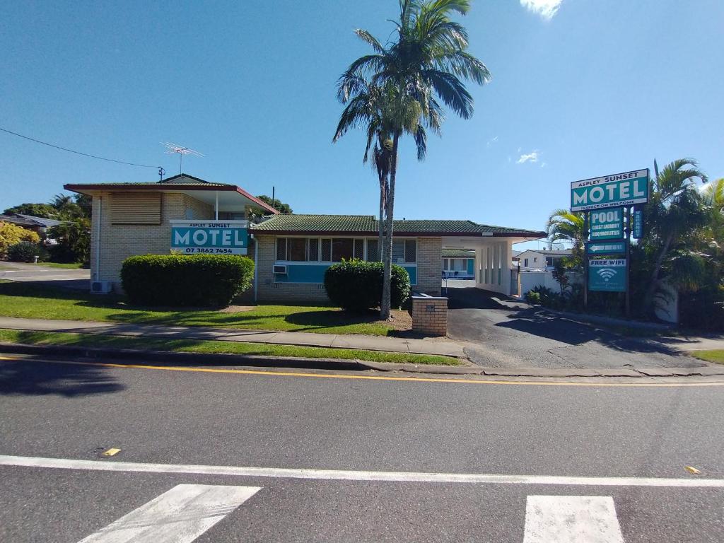 a motel with a palm tree in front of a street at Aspley Sunset Motel in Brisbane