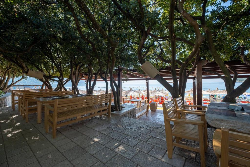 a row of wooden benches and tables with trees at Poseidon The Beach Hotel in Budva