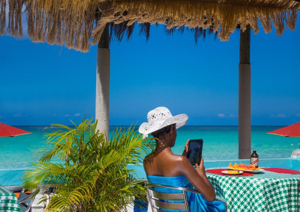 Una donna seduta su una sedia in spiaggia che guarda il suo cellulare di Legends Beach Resort a Negril