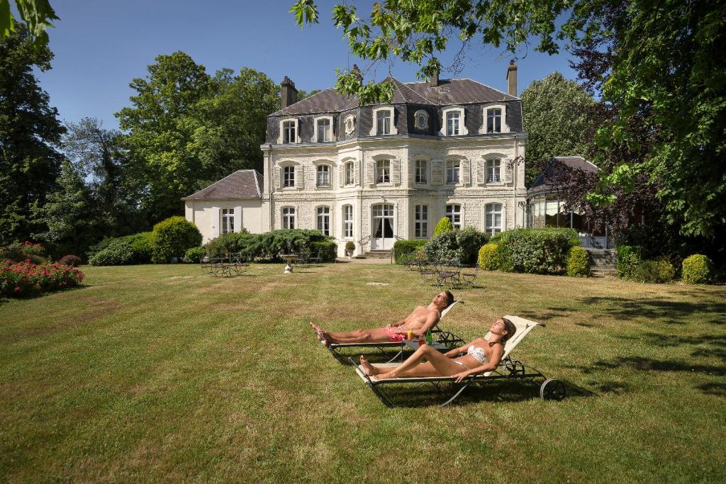 two people sitting on a bench in front of a house at Najeti Hôtel Château Cléry in Hesdin-lʼAbbé